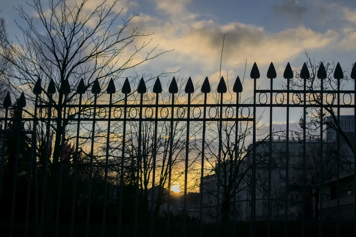 Pointed iron fence silhouetted against a winter sunset and bare trees